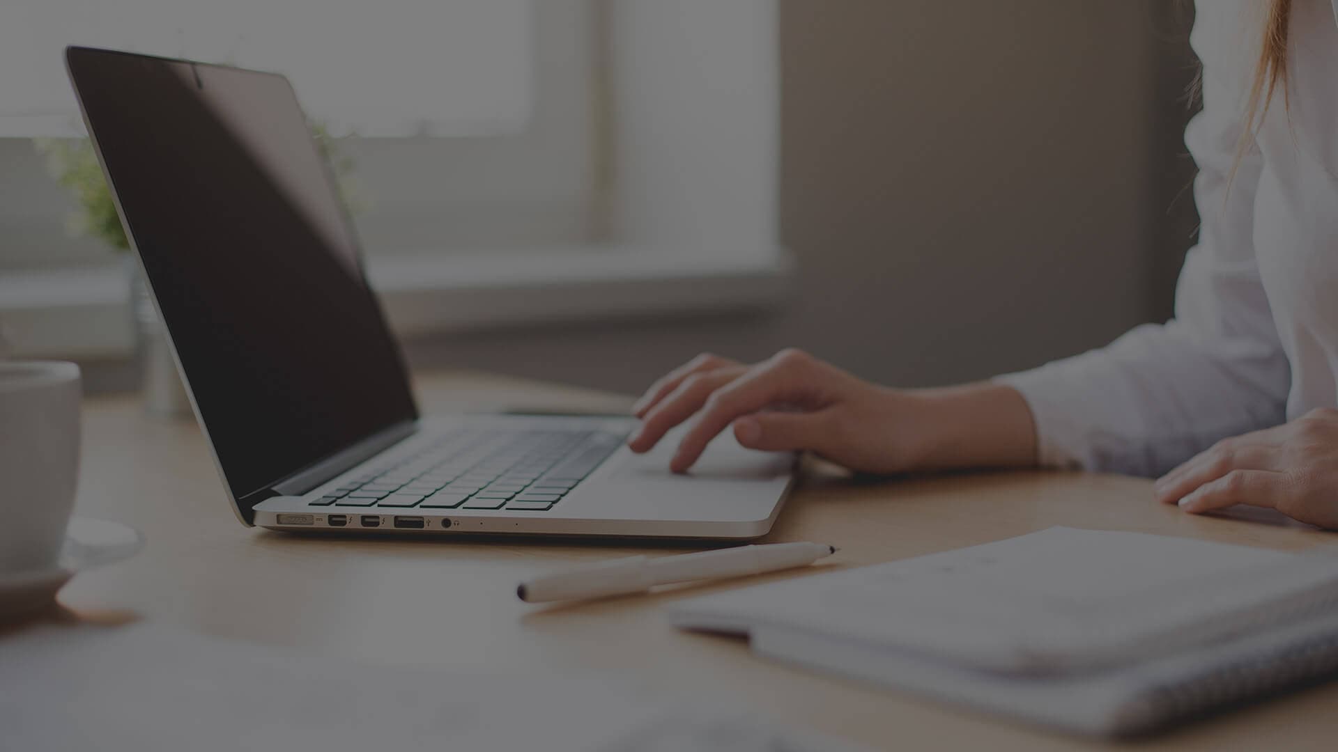 Person at a desk with one hand on the touchpad of an opened laptop.