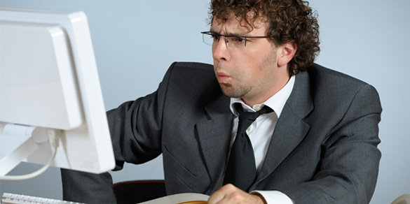 A person with pursed lips wearing a suit and looking at a computer monitor.